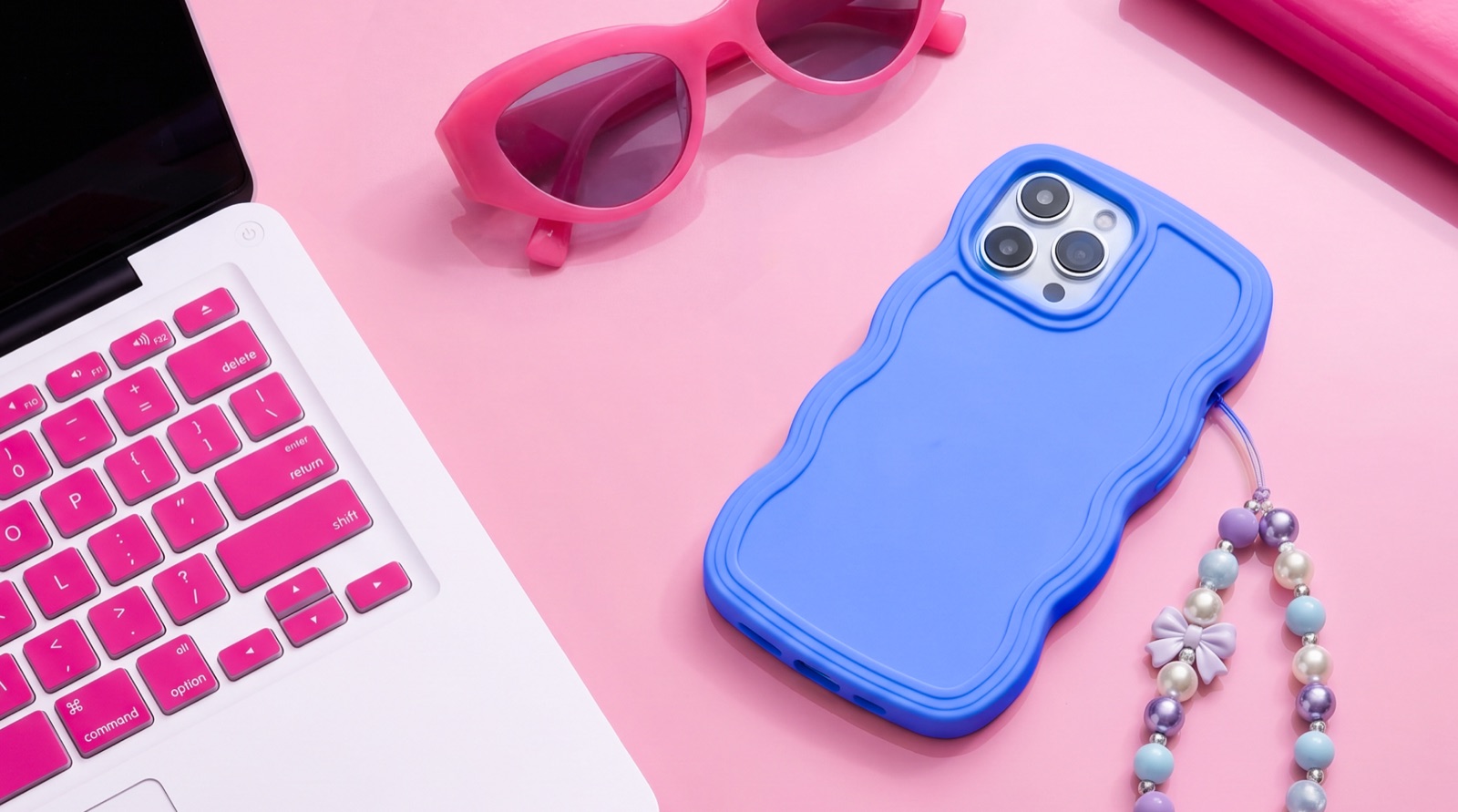 Polly lifestyle flat lay — laptop, pink sunglasses and a wavy phone case
